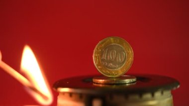 Yanan bir gaz ocağına 100 Kazak tenge madeni para