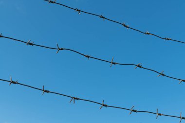 Three rows of barbed wire against the sky