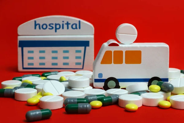 Symbolic ambulance, hospital building and various pills on a red background