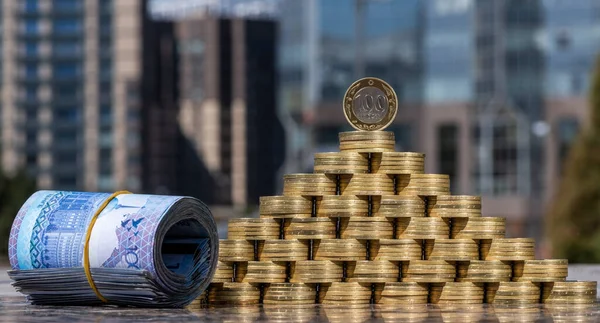 Pyramid of coins in denominations of 100 Kazakhstani tenge against the background of modern buildings