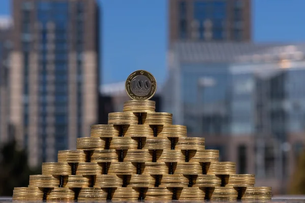 Pyramid of coins in denominations of 100 Kazakhstani tenge against the background of modern buildings