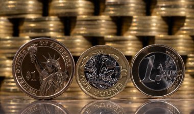 Coins of 1 American dollar, 1 British pound and 1 euro against the background of columns of gold coins