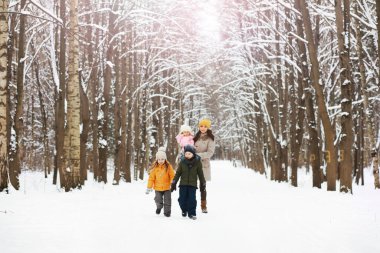 Mutlu bir aile kışın dışarıda karda oynar ve güler. Şehir parkı kış günü.