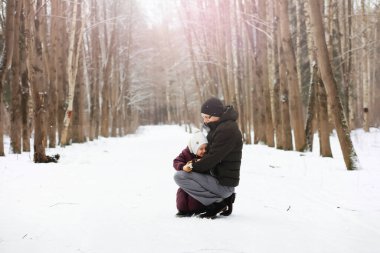 Mutlu bir aile kışın dışarıda karda oynar ve güler. Şehir parkı kış günü.