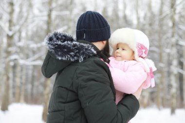 Mutlu bir aile kışın dışarıda karda oynar ve güler. Şehir parkı kış günü.