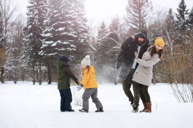 Mutlu bir aile kışın dışarıda karda oynar ve güler. Şehir parkı kış günü.