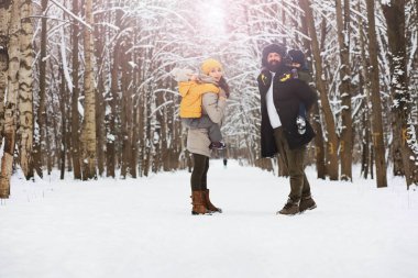 Mutlu bir aile kışın dışarıda karda oynar ve güler. Şehir parkı kış günü.