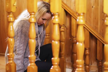 Genç bir kız kazakla merdivende oturuyor.