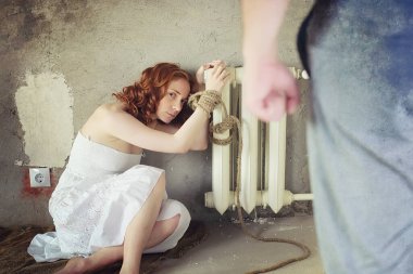 Genç kız yere bağlı. Kaçırılan kız. Şiddet kurbanı bağlı el ile katta oturuyor. Aile içi şiddet