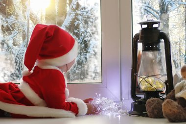 Yeni yılda bir çocuk pencereden görünüyor. Çocuklar Noel Baba için bekliyor. Noel Baba kıyafetli bir çocuğun pencerenin önünde oturur