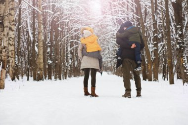 Mutlu bir aile kışın dışarıda karda oynar ve güler. Şehir parkı kış günü.