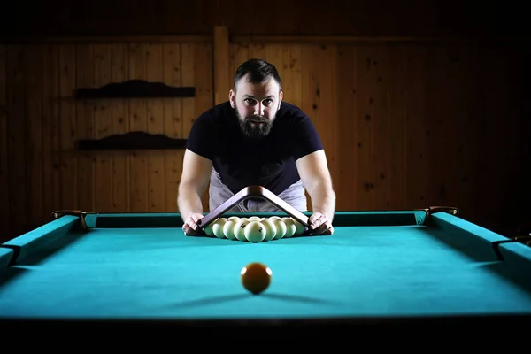 A man with a beard plays a big billiard. Party in 12-foot pool. Billiards in the club game for men. A man with a cue breaks the pyramid