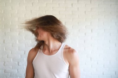 Uzun saçlı genç adam el sallıyor.  