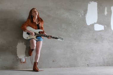 Kızıl saçlı kız elektro gitar ile. Rock müzisyen kız bir deri ceket. O güzel bir şarkıcı ve rock müzik sanatçısı.