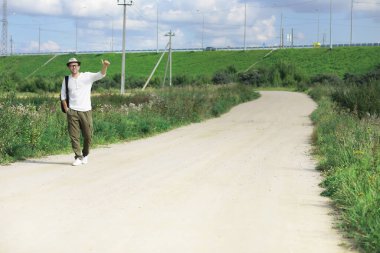Bir adam köy yolunda yürüyor. Ülkenin her yerinde otostopçu. Bir adam yoldan geçen bir arabayı durdurur..