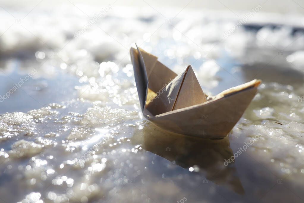Paper boat in the water on the street. The concept early spring. Melting snow and an origami boat on water waves.