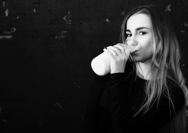 Genç kız siyah duvardaki bir şişeden süt içiyor.