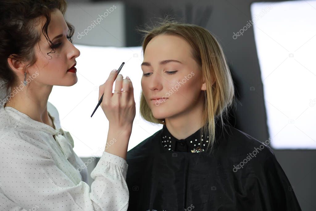 Young girl with a make-up artist in the studio in front of a mirro