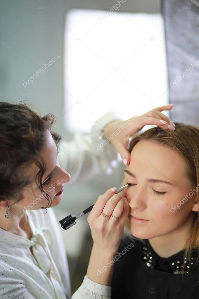 Young girl with a make-up artist in the studio in front of a mirro