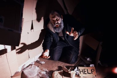 Evsiz sakallı bir adam sokakta kutulara oturup yardım istiyor. Evsiz bir insan yemek için para ister ve bir gecede.