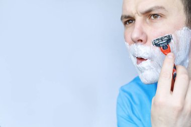 Bir adam aynanın önünde tıraş olur. Tıraş köpüğü. Tek kullanımlık jilet..