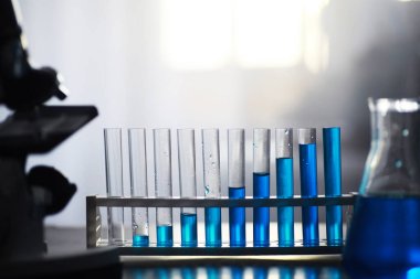 Laboratuvar masasında mavi sıvıyla test tüpü. Sıvının mikroskop altında incelenmesi.