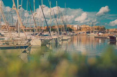 Güneşli bir günde Malta, Valletta 'da güzel bir marina manzarası. Biraz yeşillik ön planda ve kabarık bulutlar gökyüzünde.