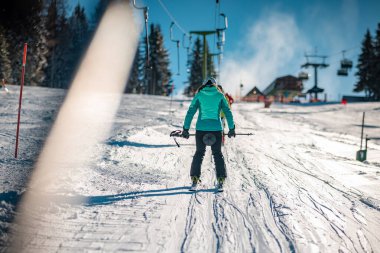 Unknown person is being pulled up by an old ski lift with rings or plates on a sunny day. Riding on a ski lift, back view of skier.
