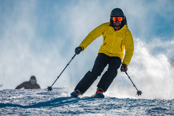 Young person in fashionable clothes is skiing towards the camera on a ski slope on a sunny day. Carve or carving on ski piste, perfect weather, strong backlight.