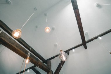 Tavandan sarkan süslü vintagy tarzı ampulleri olan, ahşap fonlarıyla desteklenen modern çatı katı tarzı bir daire..