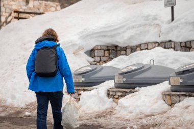 Bilinmeyen bir erkek, içinde çöp olan plastik bir poşeti köydeki geri dönüşüm kutularına ya da daha büyük çöp kutularına götürüyor..