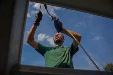 Adam çatı kenarına zift yalıtımı uygulamak için ısı tabancası ya da ısı tabancası kullanıyor ya da bir evin beton kenarına merdiven kullanarak su yalıtımı yapıyor..