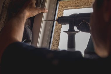 Eski bir eve modern pvc pencere veya çerçeve takmak için pilli matkap kullanan biri. Eski evin ve yeni pencerelerin yenilenmesi.