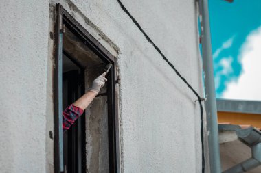 Bilinmeyen bir ressamın eli, pencere çerçevelerini taze kahverengi boyayla boyuyor. Şehir merkezindeki eski pencerelerin restorasyonu. Boya fırçasıyla görünür bir el..