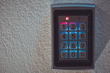 Modern dijital kombinasyon kilidinin önden görünüşü, mavi renkli aydınlatma anahtarları, kilitli kapıları gösteren kırmızı ışık..