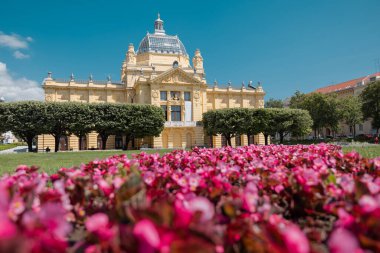 Sıcak bir yaz gününde Kralj Tomislav Parkı 'ndaki merkez zagreb' deki güzel sanat galerisi. Ön planda kırmızı çiçekli sarı bina..