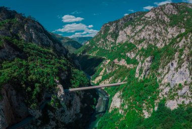 Vadi üzerindeki yüksek yol köprüsüne yakın Piva Nehri Kanyonu 'nun dar geçidi. Arka planda yeşil dikey kaya oluşumları ve mavi gökyüzü, Durmitor ve Mratinje hidroelektrik barajına yakın..