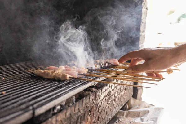 Flipping around meat on wooden sticks, algerian traditional food, over a hot charcoal grill. Smoke rising up from meat, coal below.