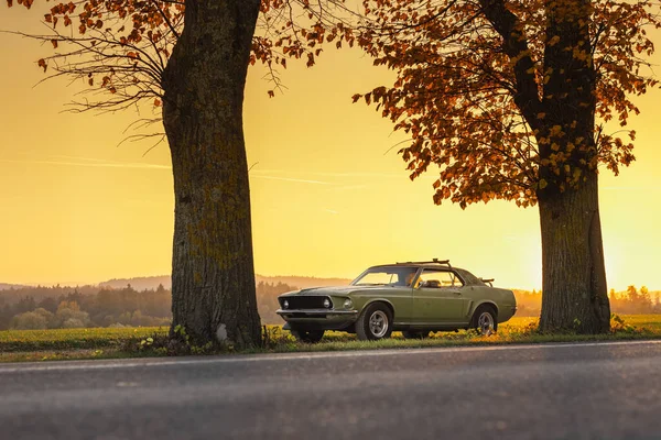 Old american muscle car in green color, photograph taken in low profile and in evening sunset with sun close to horizon. Romantic oldtimer car photo.