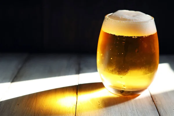 A frothy beer poured into a short, rounded glass illuminated by the strong afternoon light