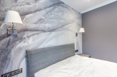The interior of the bedroom is in light gray tones with a beautiful pattern on the wall at the head of the bed.