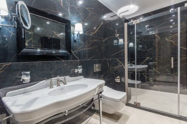 A luxurious bathroom with black marble tiles on the walls, a mirror over the sink and a large shower cabin.
