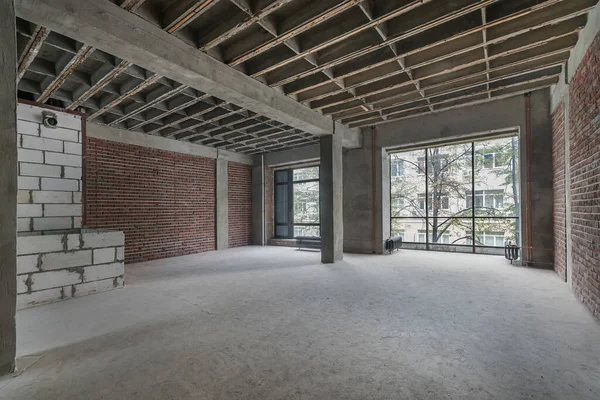 A spacious room without decoration with brick walls and large windows.