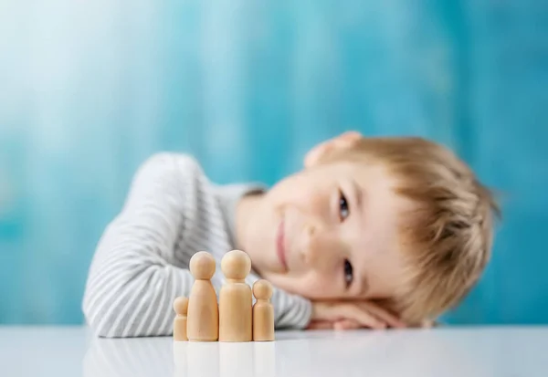 Lächelndes Kind mit Holzfiguren der Familie auf blauem Hintergrund — Stockfoto
