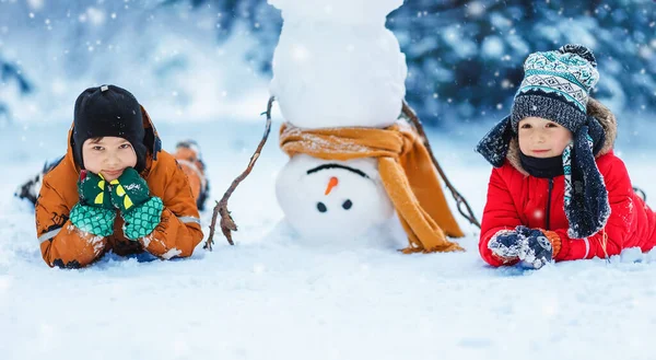 Dzieci leżące na śniegu w pobliżu zabawnego bałwana — Zdjęcie stockowe