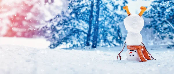 Веселый снеговик с оранжевым шарфом и в жёлтых сапогах стоит вверх ногами в зимнем лесу — стоковое фото