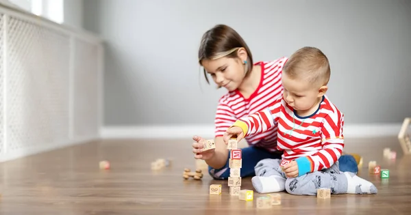 Schwester und Bruder spielen gemeinsam mit Würfeln auf dem Fußboden im Haus. — Stockfoto