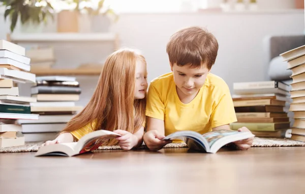 Dos niños lindos tumbados en el suelo con libros en la cabeza — Foto de Stock