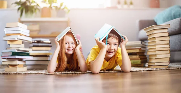 Zwei niedliche Kinder liegen drinnen mit Büchern auf dem Kopf auf dem Boden — Stockfoto