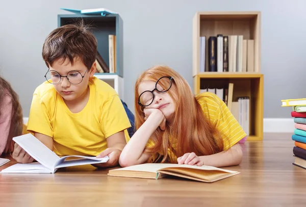 Милі діти в окулярах лежать на підлозі в приміщенні з книгами — стокове фото